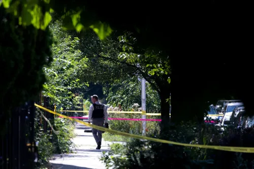 شرطي يسير في منطقة محاطة بالأشجار، مع وجود شريط تحذيري، في سياق تقرير عن انخفاض الجرائم العنيفة في الولايات المتحدة.