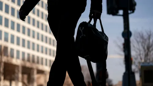 رجل يسير في الشارع حاملاً حقيبة، مع خلفية مباني تعكس حالة عدم اليقين الاقتصادي والقلق بشأن البطالة.