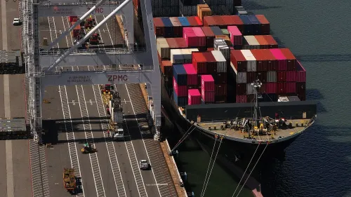 سفينة شحن محملة بالحاويات الملونة في ميناء، تعكس تأثيرات الحرب التجارية على الاقتصاد الأمريكي وسوق العمل.