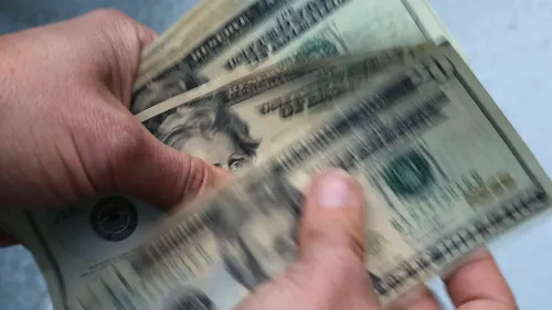 يد تُمسك بعدة أوراق نقدية من فئة عشرين دولارًا، مما يعكس مشهدًا يتعلق بالعجز الفيدرالي والضغوط المالية في الكونغرس.