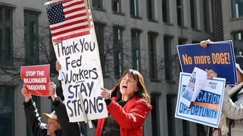 محتجون يحملون لافتات تدعم حقوق العمال الفيدراليين، مع امرأة ترتدي سترة حمراء وتحتج بصوت عالٍ.