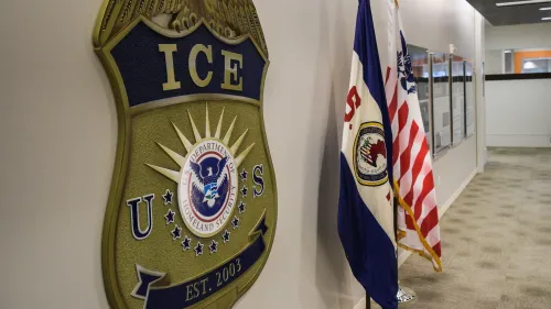 شعار إدارة الهجرة والجمارك الأمريكية مع أعلام الولايات المتحدة، في مكتب إداري، يعكس قضايا الترحيل والمهاجرين.