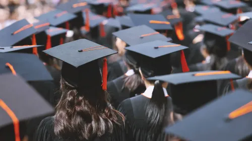 حفل تخرج يضم مجموعة من الطلاب يرتدون قبعات التخرج والعباءات، مع التركيز على تفاصيل القبعات المميزة بشريط برتقالي.