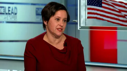 امرأة تتحدث في استوديو تلفزيوني، مع العلم الأمريكي خلفها، تناقش التحديات القانونية للموظفين الفيدراليين في ظل تسريحات الحكومة.