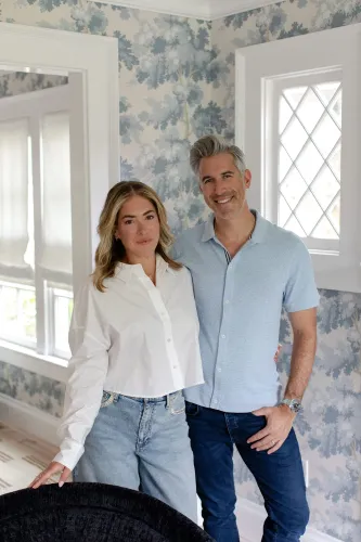 زوجان يقفان معًا في غرفة ذات جدران مزينة بأزهار، يعكسان الثقة والتعاون في التعامل مع القضايا المالية في علاقتهما.