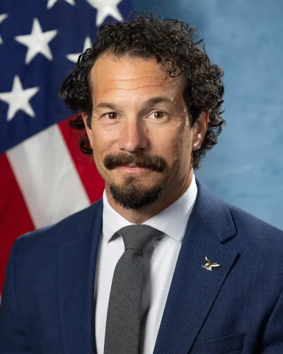 صورة لرجل يرتدي بدلة رسمية مع ربطة عنق، يقف أمام علم أمريكي، ويبدو أنه أحد كبار مسؤولي مكتب التحقيقات الفيدرالي السابقين.