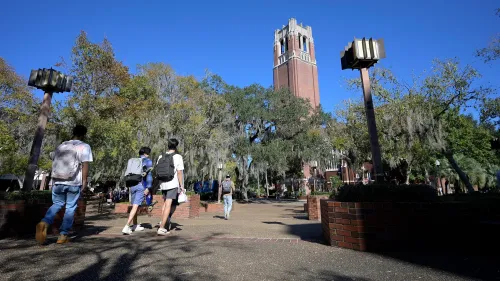 طلاب يسيرون في حرم جامعة فلوريدا تحت برج مميز، في سياق تزايد القلق بشأن قوانين الهجرة وتأثيرها على الطلاب الدوليين.