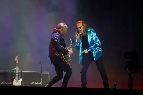 أعضاء فرقة Maná يؤدون على المسرح، مع التركيز على المغني الرئيسي وعازف الجيتار، في أجواء موسيقية حماسية تعكس روح جولة _Vivir Sin Aire_.