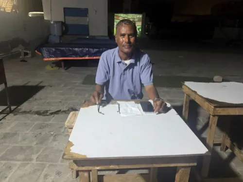 رجل مسن يجلس على طاولة خشبية في ملعب محلي بمُكلَّا، يراقب مباراة كأس العالم 2026، بينما يعبر عن شغفه لكرة القدم رغم التحديات.