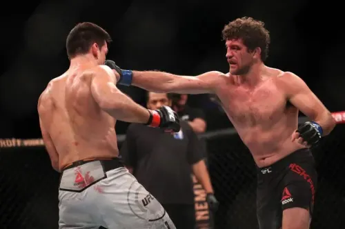 مقاتل الفنون القتالية المختلطة بن أسكرين يوجه ضربة لمنافسه خلال نزال في UFC، مع وجود حكم في الخلفية.