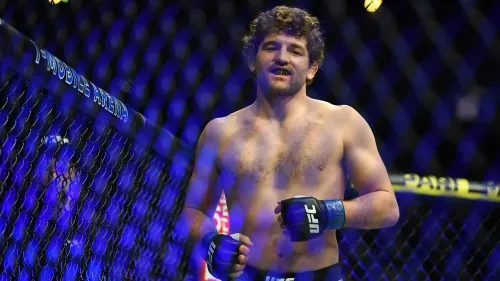 بن أسكرين، مقاتل سابق في UFC، يظهر مبتسمًا في الحلبة بعد انتصاره، مع خلفية مضاءة بألوان زاهية.