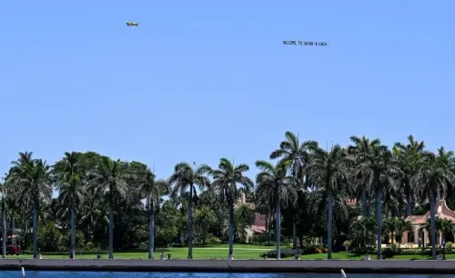 طائرة صغيرة تحمل لافتة ترحيبية فوق منتجع ترامب في فلوريدا، محاطة بأشجار النخيل، في سياق مناقشات حول الفساد المحتمل.
