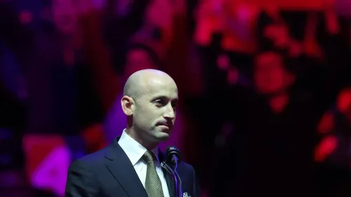 ستيفن ميلر يتحدث في تجمع انتخابي، مرتديًا بدلة، مع حشود خلفه. يبرز دوره كأحد أبرز مستشاري ترامب في تنفيذ سياسات الهجرة.