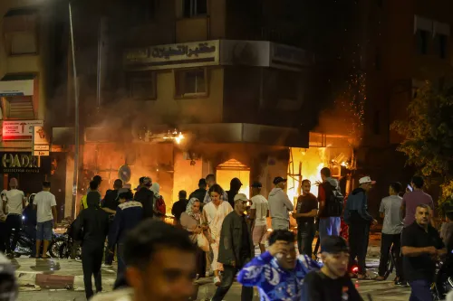 محتجون شباب في المغرب يتجمعون في الشوارع خلال احتجاجات ضد الأوضاع الاقتصادية، مع اندلاع النيران في خلفية الصورة.