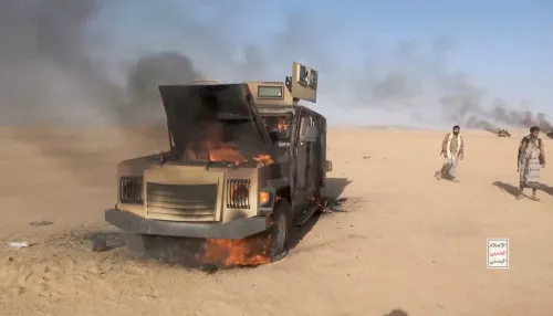 دبابة عسكرية محترقة وسط الصحراء مع مسلحين حوثيين في تقدم نحو مضيق باب المندب في اليمن، يعكس تصاعد النزاع وتأثيره على الأمن الإقليمي.