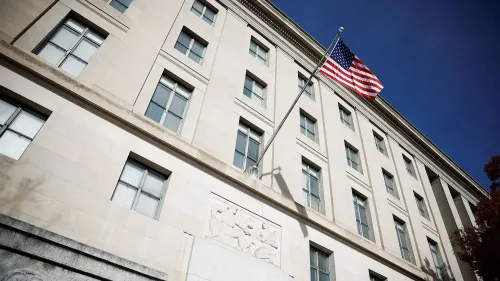 واجهة مبنى حكومي يظهر عليها علم الولايات المتحدة، مع تفاصيل معمارية بارزة تبرز في السماء الزرقاء.