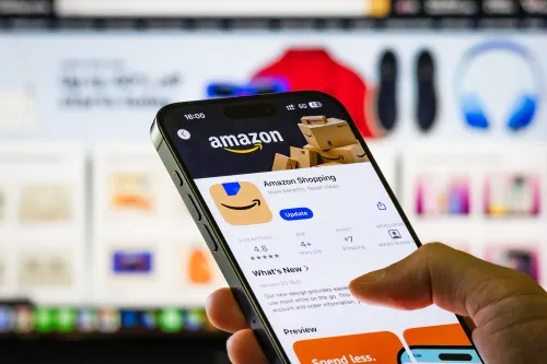 شخص يستخدم تطبيق أمازون على هاتف ذكي مع خلفية تعرض منتجات إلكترونية، في سياق قضايا التلاعب بأسعار الإعلانات الرقمية.