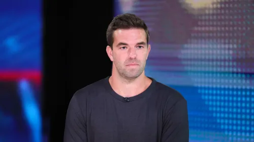 بيلي ماكفارلاند يتحدث في برنامج تلفزيوني، مع خلفية ملونة، حول تأجيل مهرجان Fyre Fest 2 بسبب عدم تحديد موقع جديد.