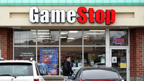 متجر GameStop يظهر في الصورة، مع لافتة كبيرة تحمل الاسم، حيث يتواجد شخص أمام المتجر. تعكس الصورة التحديات التي تواجه الشركة في ظل إغلاق المتاجر وتحولها نحو العملات الرقمية.