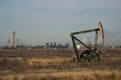 مضخة نفط تعمل في حقل نفطي، مع وجود منشآت صناعية في الخلفية، تعكس تأثير تقلبات أسعار النفط على الاقتصاد الأمريكي.