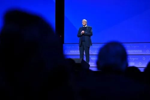 بيل غيتس يتحدث على المسرح خلال حدث يركز على صحة المرأة، مع خلفية زرقاء وشعارات تدعم أهداف التقدم.