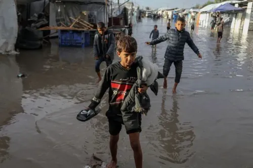 أطفال يتجولون في مخيم للنازحين في غزة، حيث غمرت المياه الخيام بسبب الأمطار الغزيرة، مما يزيد من معاناة الأسر النازحة.