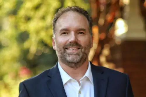 إريك جيسلر، مرشح ديمقراطي لمجلس النواب في ولاية جورجيا، مبتسم في صورة رسمية، مع خلفية طبيعية خضراء.