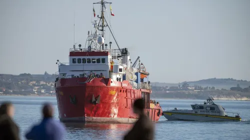 سفينة إنقاذ حمراء كبيرة تقترب من الساحل، ترافقها قارب تابع للشرطة، في إطار جهود إنقاذ المهاجرين في البحر الأبيض المتوسط.