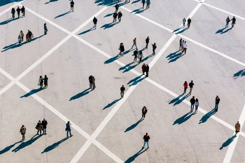 صورة تظهر مجموعة من الأشخاص يتجولون في ساحة مفتوحة، مع ظلالهم الممتدة على الأرض. تعكس الصورة التغيرات في معدلات الوفيات والصحة العامة.