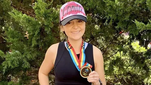 صورة لامرأة مبتسمة ترتدي قبعة تحمل كلمة \"LDANG\" وتستعرض ميدالية ملونة، تعكس إنجازاتها في سباقات الجري.