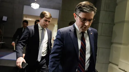 رجلان يرتديان بدلات رسمية، يسيران معًا في مبنى حكومي، مع تعبيرات جدية تعكس التوترات السياسية حول ميزانية الكونغرس.