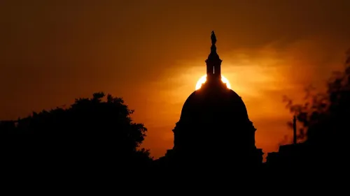 غروب الشمس خلف قبة مبنى حكومي، مع silhouette لشجرة وأعلى القبة، مما يعكس أجواء سياسية متوترة في أوقات التخفيضات المالية.