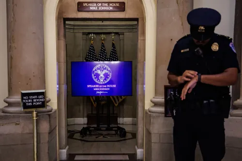 صورة تظهر ضابط أمن يقف بجانب شاشة تعرض اسم رئيس مجلس النواب مايك جونسون، مع العلم الأمريكي في الخلفية.