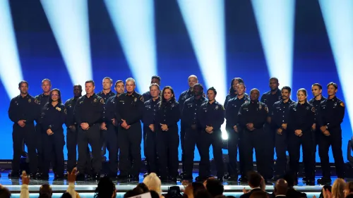 مجموعة من رجال الإطفاء والموظفين في زيهم الرسمي يقفون على المسرح أثناء حفل توزيع جوائز غرامي، مع أضواء ساطعة خلفهم.