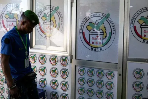 رجل يرتدي زيًا رسميًا يقف أمام مركز الانتخابات في غينيا، حيث تظهر شعارات الانتخابات على الجدران، في سياق الاستفتاء الدستوري.