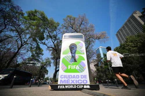 لافتة تحمل شعار كأس العالم في المكسيك، مع مشهد حضري يتضمن أشجارًا ومباني، تعكس الاستعدادات للبطولة وسط تساؤلات حول الأمن.