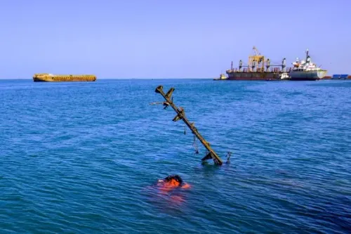 سفينة تجارية غارقة جزئيًا في البحر الأحمر، مع وجود حطام وناقلات أخرى في الخلفية، تعكس آثار الهجوم الحوثي.