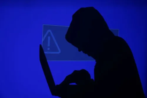 شخصية مظللة تحمل جهاز كمبيوتر محمول، مع خلفية زرقاء تظهر علامة تحذير، تعكس تأثير الهجوم الإلكتروني على منصة Canvas التعليمية.