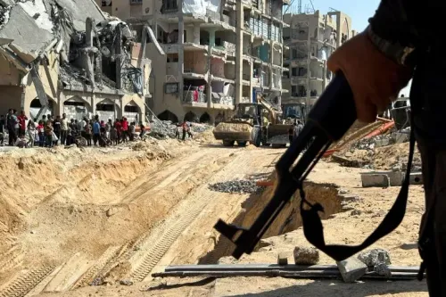 مسلح يحمل سلاحه في غزة، بينما تظهر في الخلفية المباني المدمرة وأعمال إعادة الإعمار، مع تجمع للناس في المنطقة.