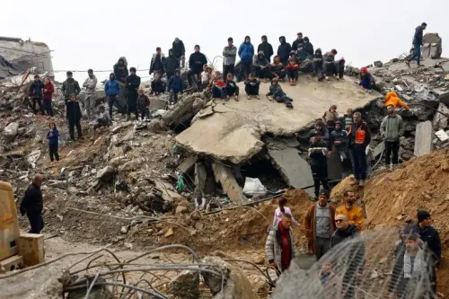 مجموعة من الأشخاص يتجمعون حول أنقاض مبنى مهدوم في غزة، يعكس تأثير الهجمات الإسرائيلية المستمرة على المدنيين.