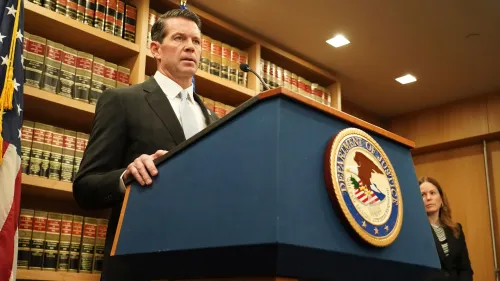 جيمس دينيهي يتحدث في مؤتمر صحفي، مع خلفية تحتوي على كتب قانونية وشعار وزارة العدل الأمريكية، بعد إعلانه عن تقاعده.
