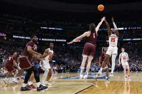 لاعب من فريق مونتانا يسدد كرة ثلاثية بينما يحاول لاعب من فريق ويسكونسن الدفاع عنه، في مباراة مثيرة ببطولة NCAA.