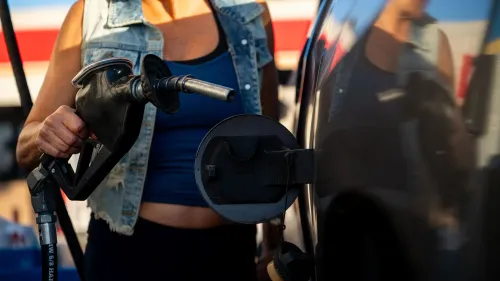 امرأة تمسك بمضخة وقود أثناء تعبئة سيارتها بالبنزين، تعكس أسعار الوقود المستقرة في عطلة يوم الذكرى.