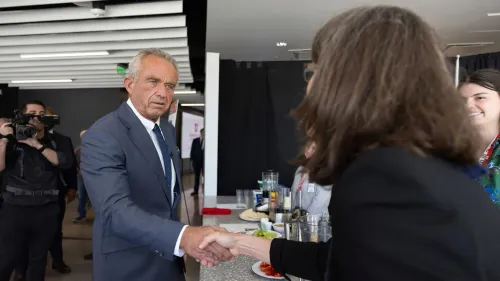 روبرت ف. كينيدي جونيور يتصافح مع امرأة خلال حدث، مع وجود مصورين في الخلفية، في سياق مناقشات حول الفلورايد في مياه الشرب.