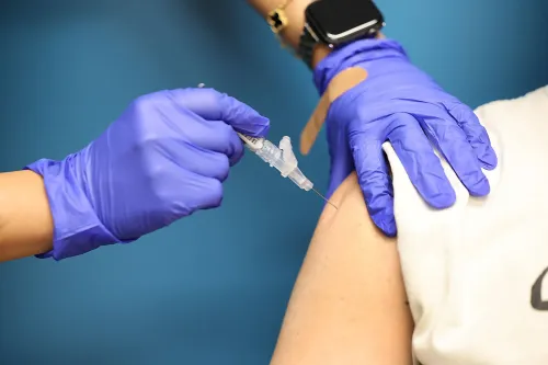 لقاح Covid-19 يُعطى في ذراع شخص يرتدي قميصًا أبيض، مع وجود طبيب يرتدي قفازات زرقاء، مما يعكس جهود التطعيم ضد الفيروس.