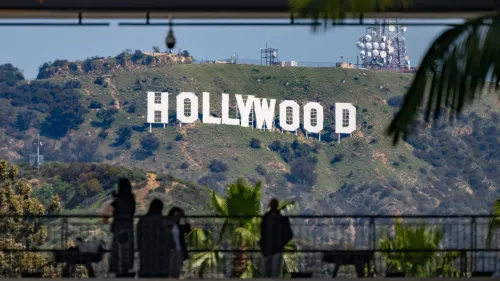 علامة هوليوود الشهيرة تظهر على تل، مع أشخاص يتجولون في المقدمة، تعكس الجدل حول التعريفات الجمركية على الأفلام الأجنبية.