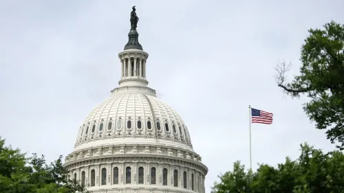 قبة مبنى الكابيتول الأمريكي تبرز تحت سماء غائمة، مع العلم الأمريكي يرفرف بجانبها، مما يعكس أجواء النقاشات السياسية حول مشروع قانون ترامب.