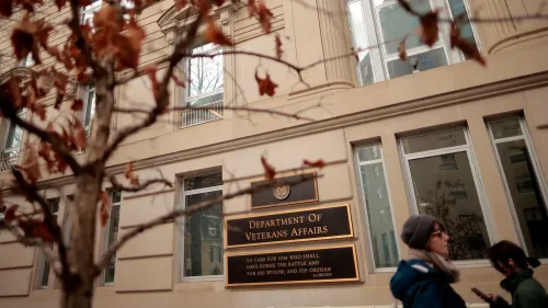 مبنى وزارة شؤون المحاربين القدامى يظهر في الصورة، مع أشخاص يسيرون بجواره، مما يعكس التحديات المتعلقة بالإسكان للمحاربين القدامى.