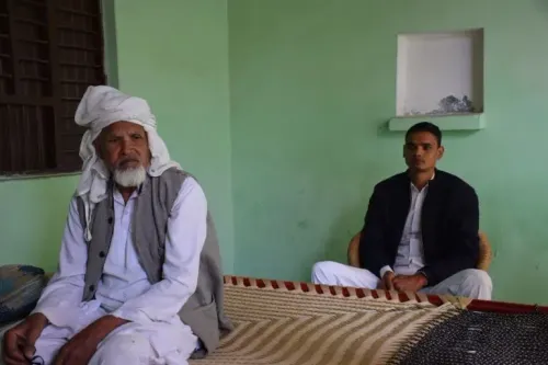 رجل مسن يرتدي عمامة يجلس في غرفة ذات جدران خضراء، بينما يجلس شاب بجانبه، مع تفاصيل بسيطة مثل سرير ونافذة صغيرة.