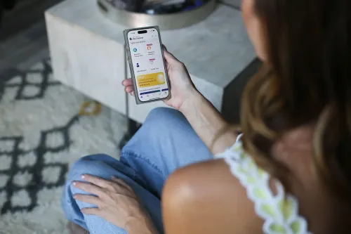 امرأة تحمل هاتفًا ذكيًا وتعرض نتائج تحليل الحمض النووي من 23andMe، بينما تجلس على أريكة في منزلها.